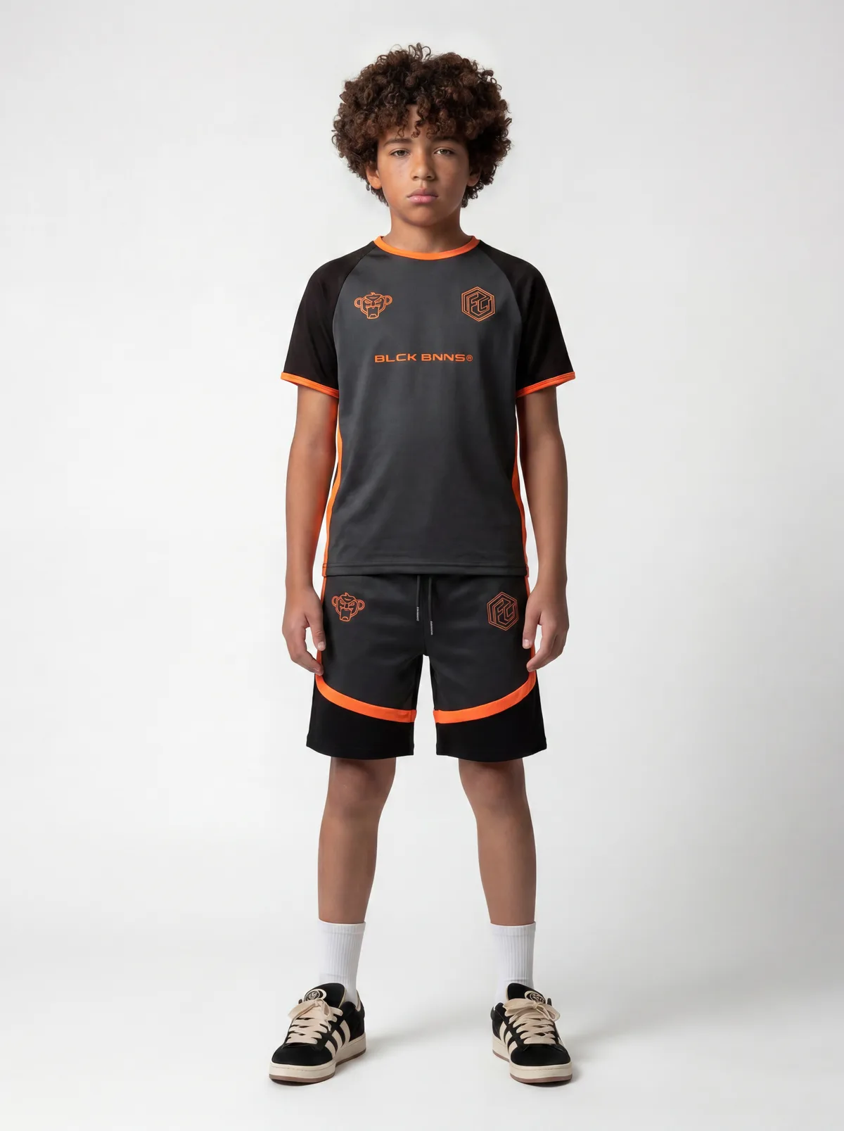 Black Bananas FC-style orange-and-charcoal football jersey with matching ringer shorts on AI young model in clean white studio