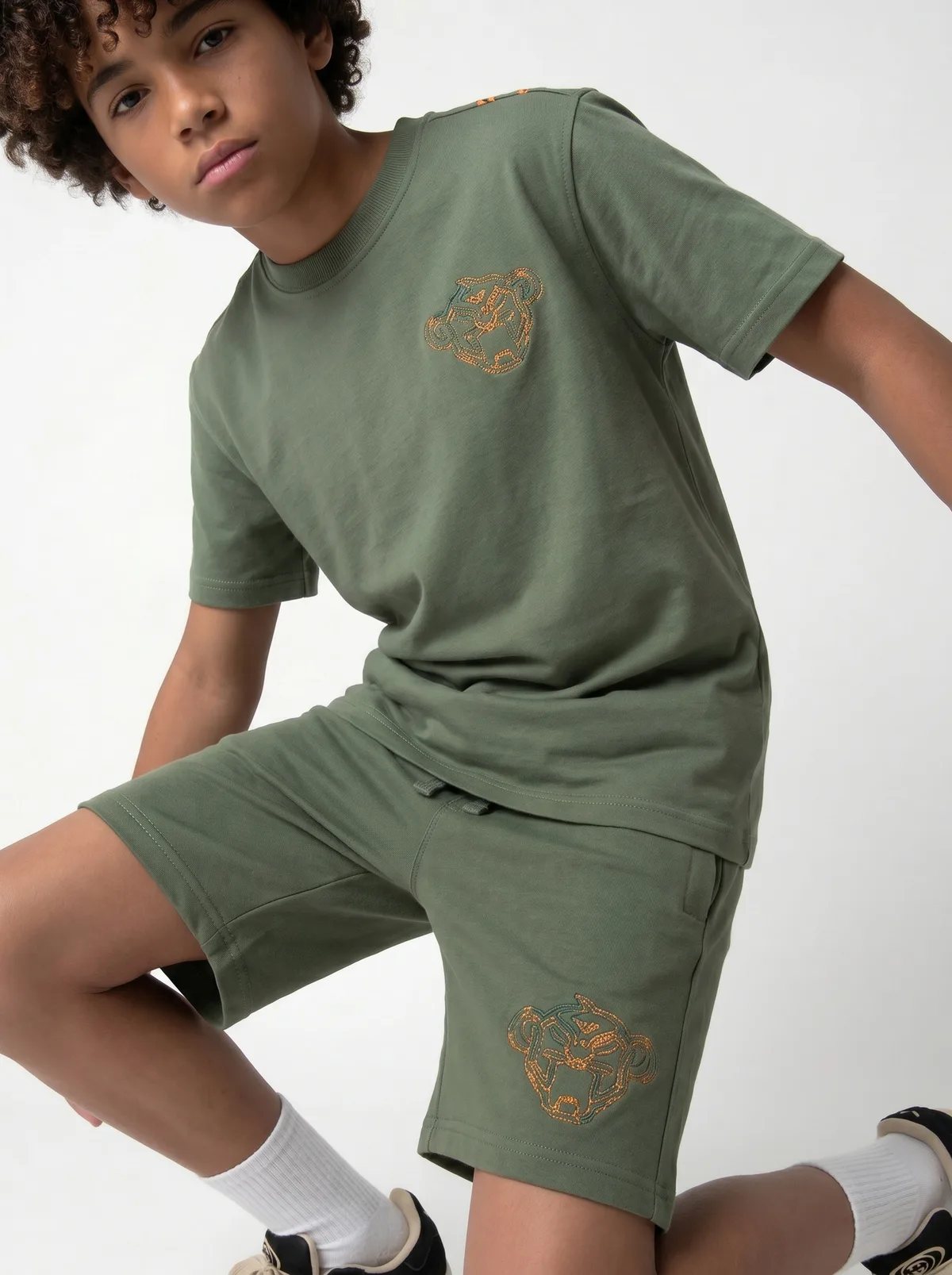 Black Bananas olive green panther tee dynamic kneeling pose on AI young model in clean studio