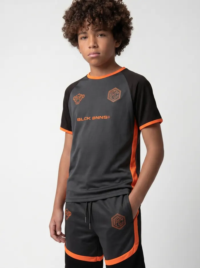 Black Bananas FC-style orange-and-charcoal football jersey alt pose on AI young model in clean white studio