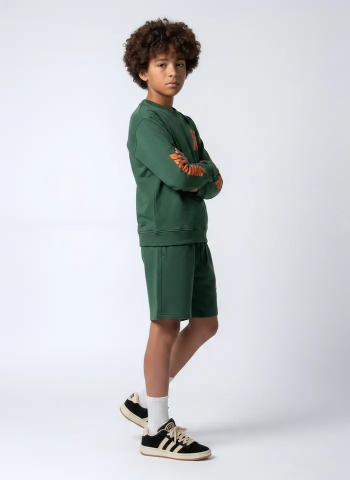 Black Bananas forest green BLCK BNNS orange-print long-sleeve and shorts twinset alt pose on AI young model in clean studio