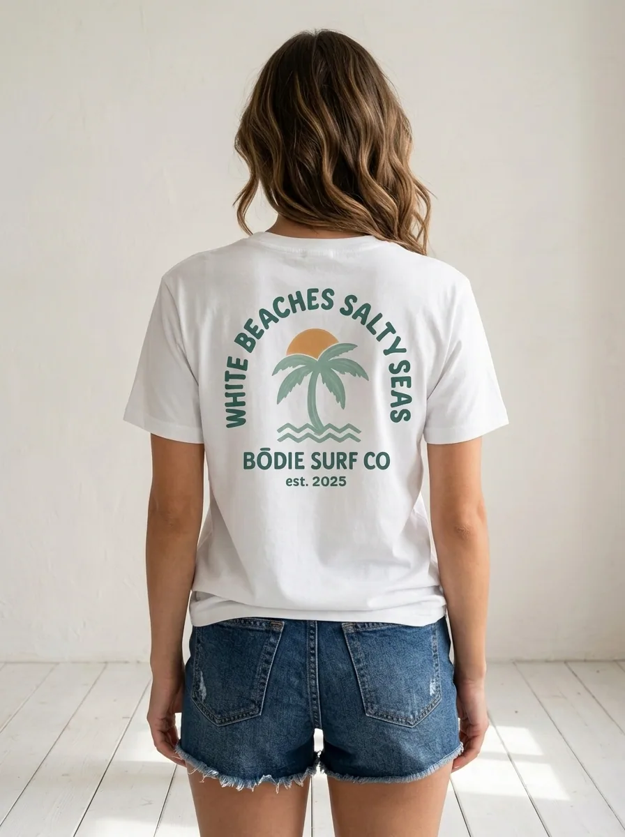 Bōdie Surf Co WHITE BEACHES SALTY SEAS back graphic with arched type, palm tree, sunset, and waves on AI female model in white studio