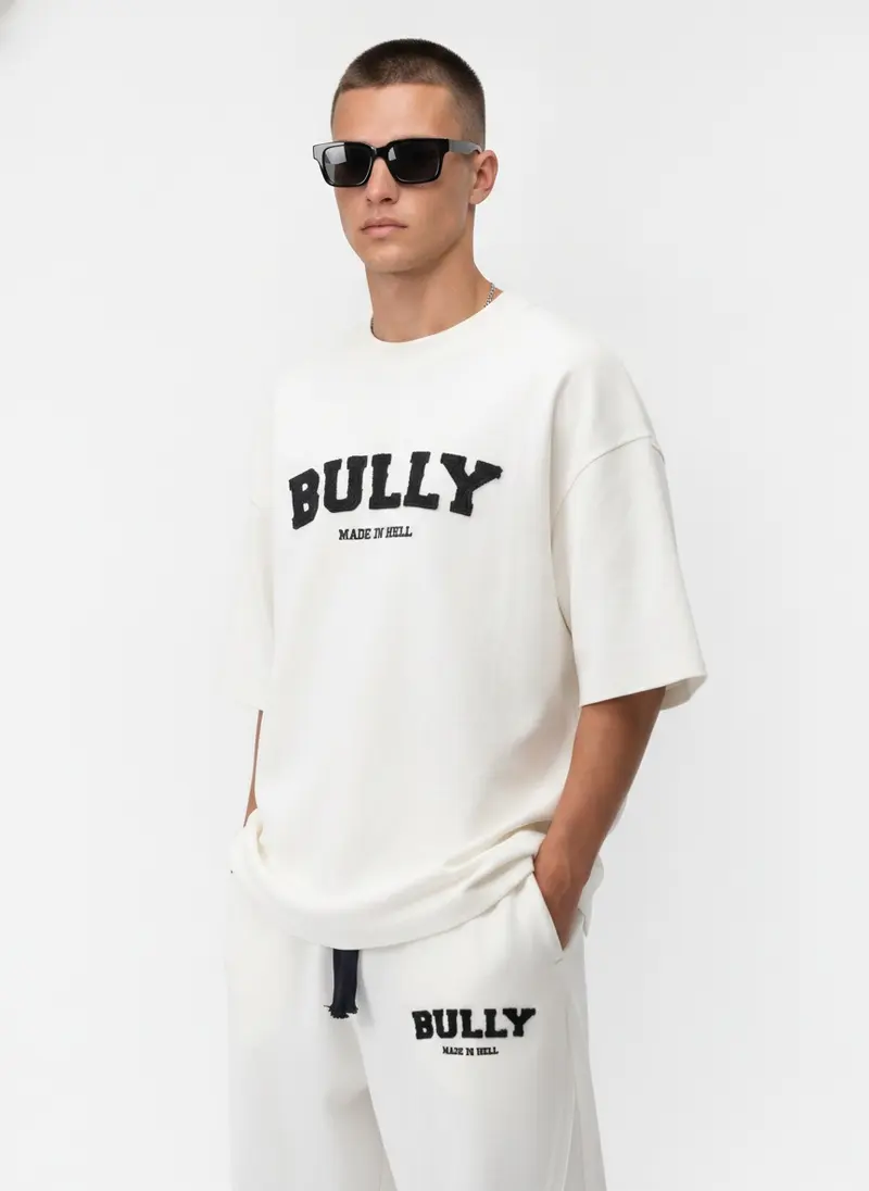 Bully Made In Hell cream co-ord set, hand-in-pocket editorial pose in a bright white studio