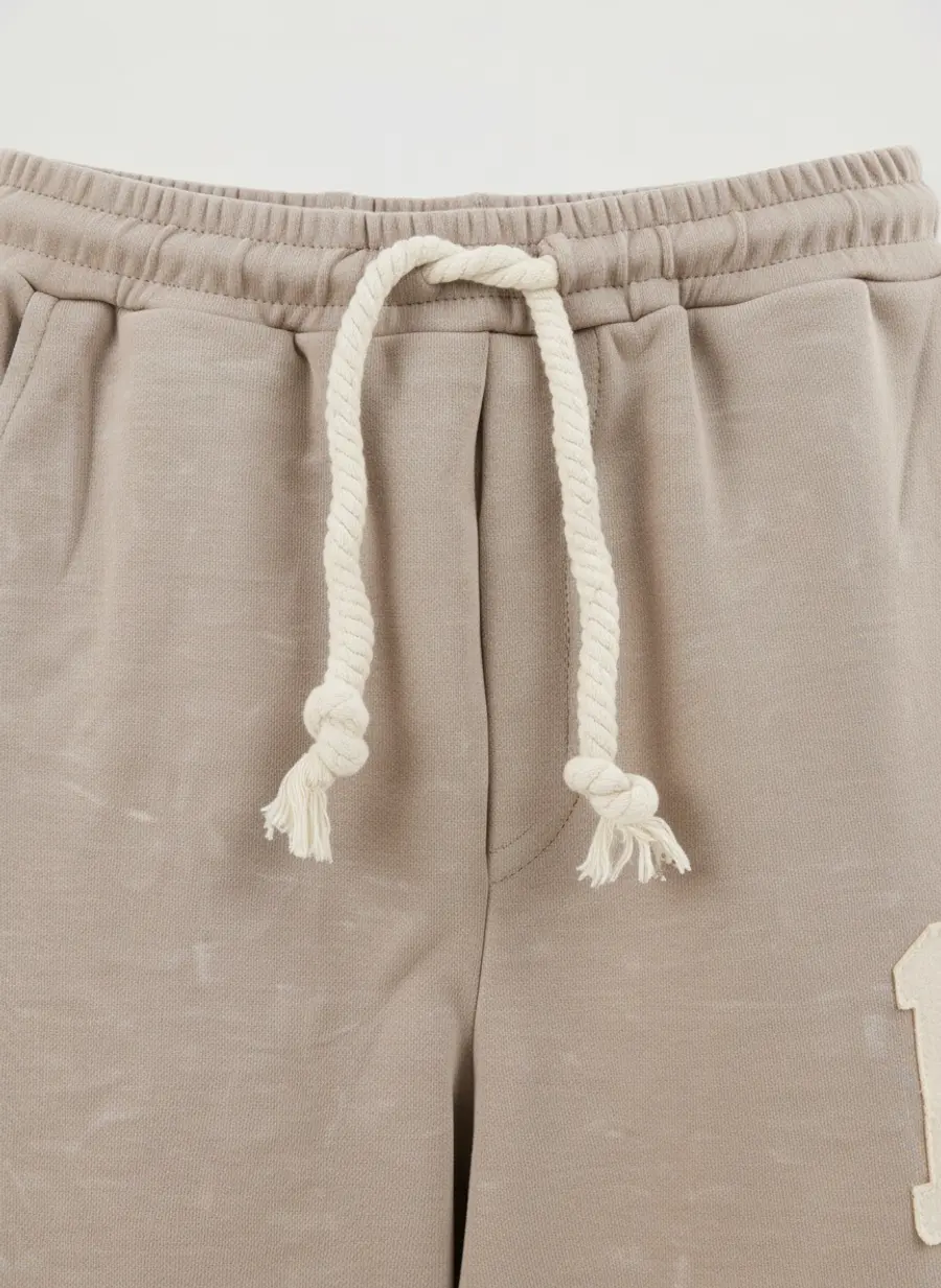 Bully sand sweatpant waistband macro showing the chunky rope drawcord, elasticated waist and the edge of the appliqué 17