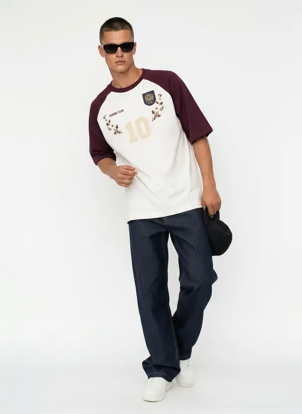 Bully Essence Club cream and burgundy raglan tee, walking three-quarter frame, on an AI male model
