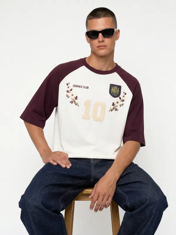 Bully Essence Club cream and burgundy raglan tee, seated editorial pose on a stool