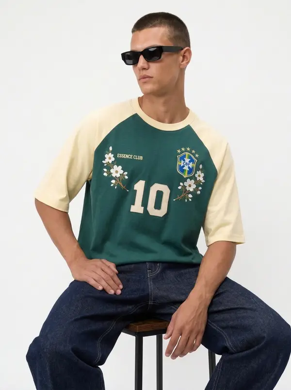 Bully Essence Club green and cream raglan tee, seated editorial pose