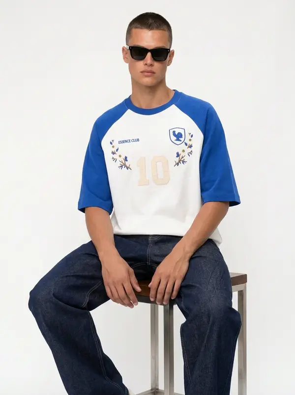 Bully Essence Club white and royal raglan tee, seated editorial pose