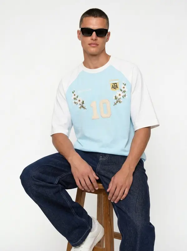 Bully Essence Club sky blue raglan tee, seated editorial pose