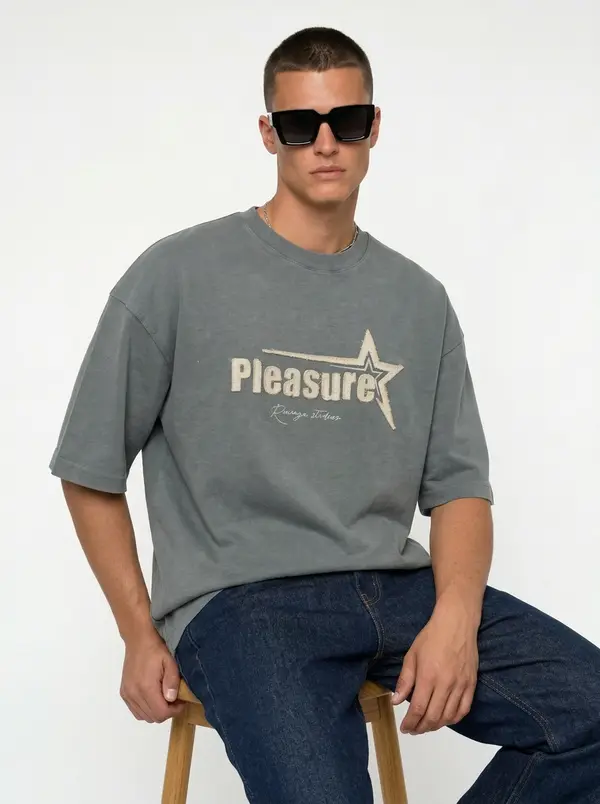 Bully Pleasure sage oversized tee, seated editorial pose with dark denim
