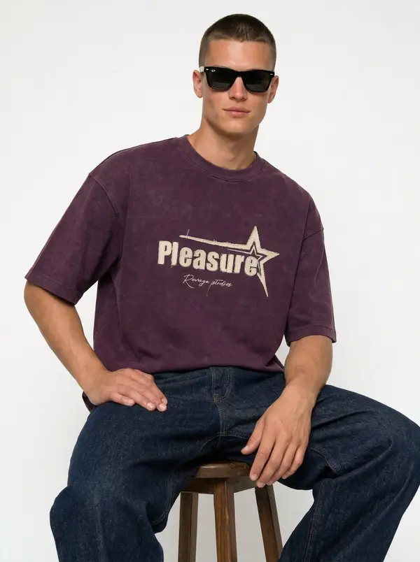 Bully Pleasure plum oversized tee, seated editorial pose with indigo denim