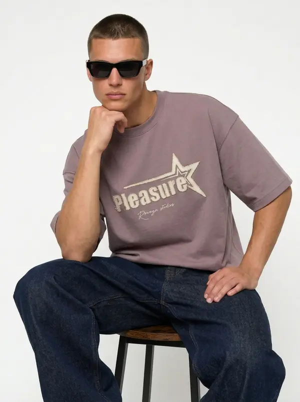 Bully Pleasure mauve oversized tee, seated editorial pose with indigo denim