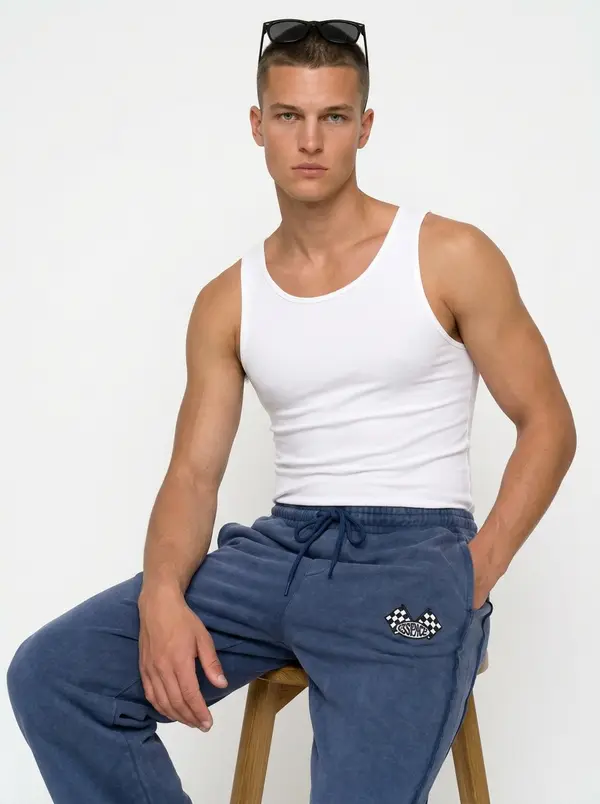 Bully washed denim blue checkered-flag sweatpant, seated editorial pose with a white tank