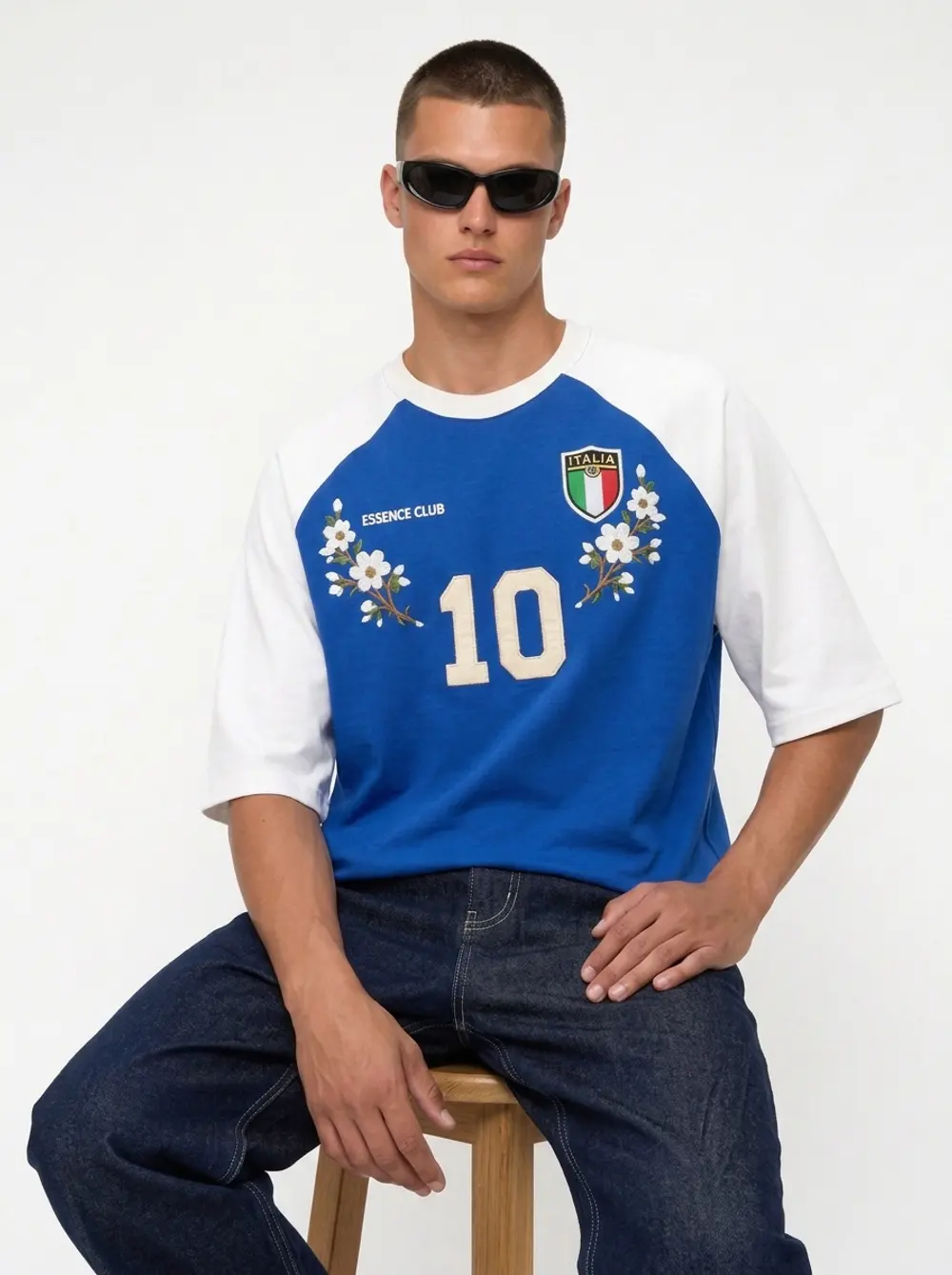 Bully Essence Club raglan tee, seated editorial pose on a stool, on an AI male model in black sunglasses