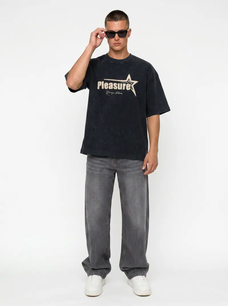 Bully Pleasure star-graphic oversized tee in washed black with grey denim, on an AI male model in a bright white studio
