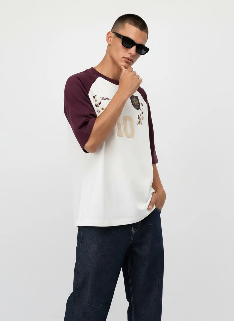 Bully Essence Club raglan tee in cream with burgundy sleeves, embroidered crest and appliqué number 10, on an AI male model