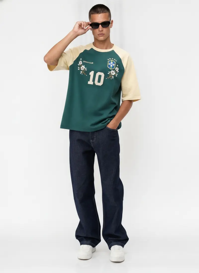 Bully Essence Club raglan tee in green with cream sleeves and an embroidered Brazil-style crest, on an AI male model