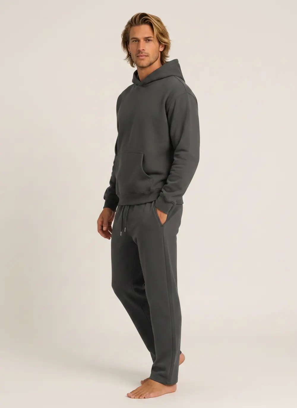 Future Homme graphite hoodie and jogger set, three-quarter turn with hand in pocket, on an AI male model in a warm studio