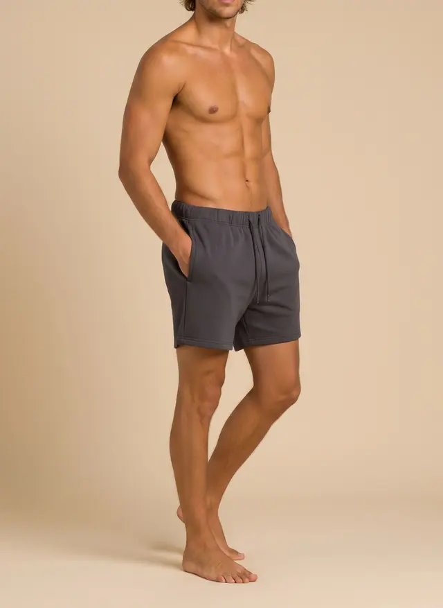 Future Homme graphite lounge short, three-quarter turn with a hand in the pocket, on an AI male model in a warm studio