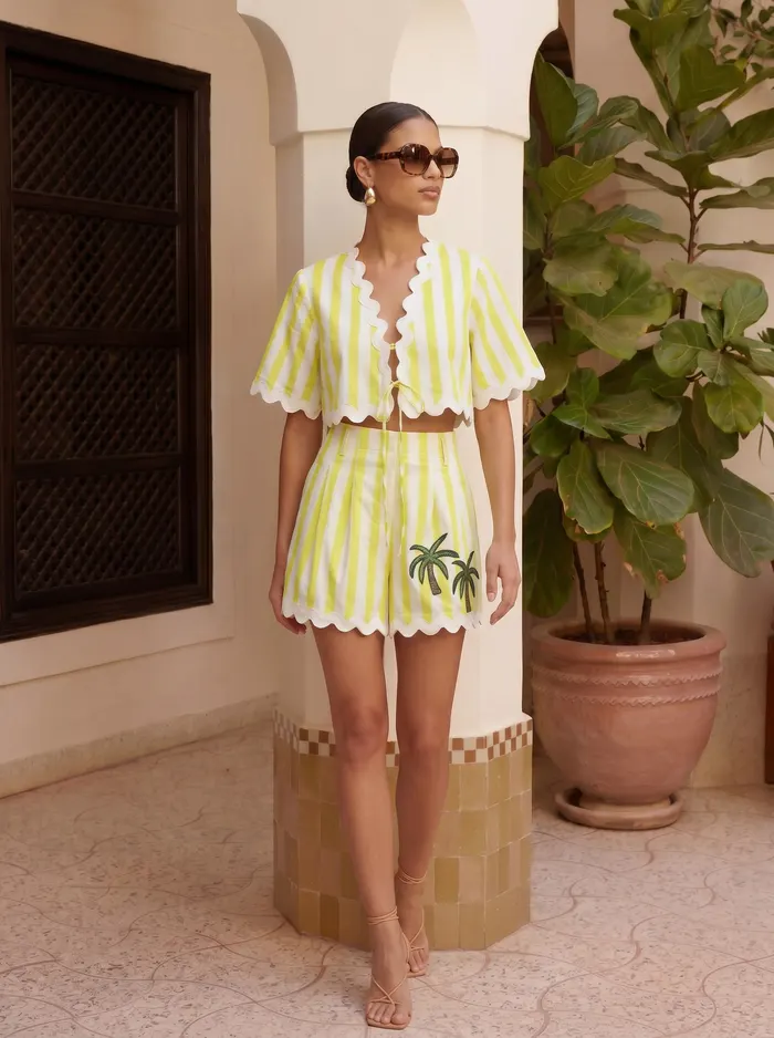 Maison Blu lime scallop crop and short set seated editorial pose with tortoiseshell sunglasses on AI model in Moroccan courtyard