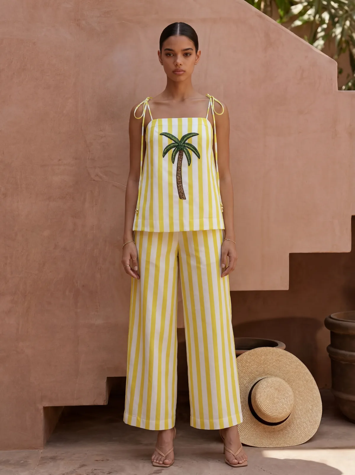 Maison Blu yellow stripe palm-front halter tank with matching wide-leg pants on AI model in terracotta courtyard, straw hat propped beside