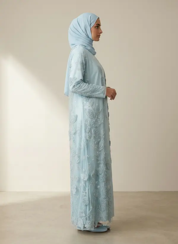 Modest Valoria powder blue abaya set, side profile full length, on an AI model in a sunlit plaster room