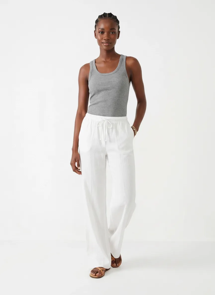 MODA AI editorial — Black model in gray ribbed tank and white linen pants in a clean studio backdrop, demonstrating professional catalog imagery generated from a Shopify boutique's iPhone source photos under the new AI labeling laws
