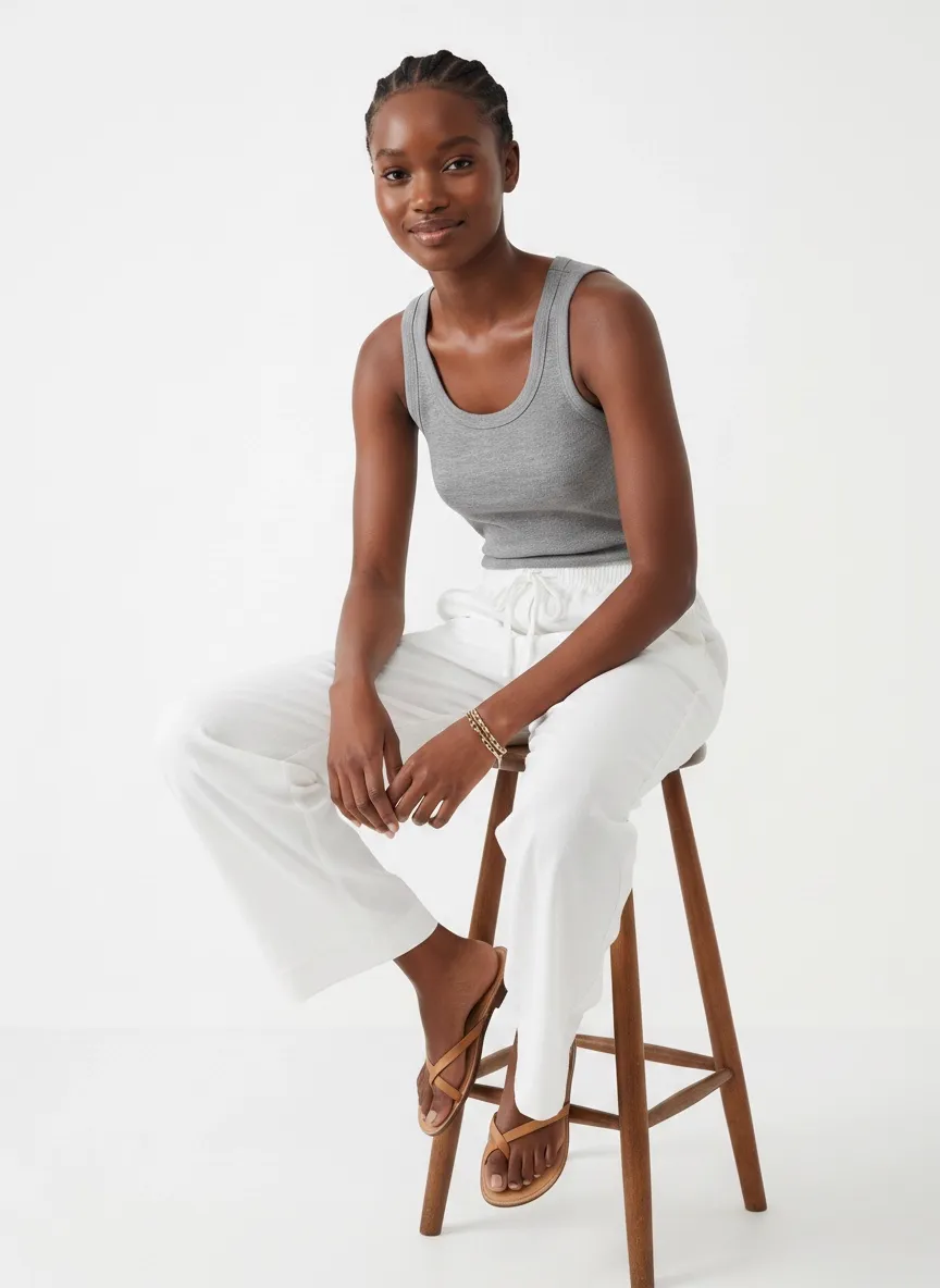 MODA AI catalog output — Black model seated on wooden stool in gray tank and white linen pants, editorial cohesion with the walkthrough 1 stool frame