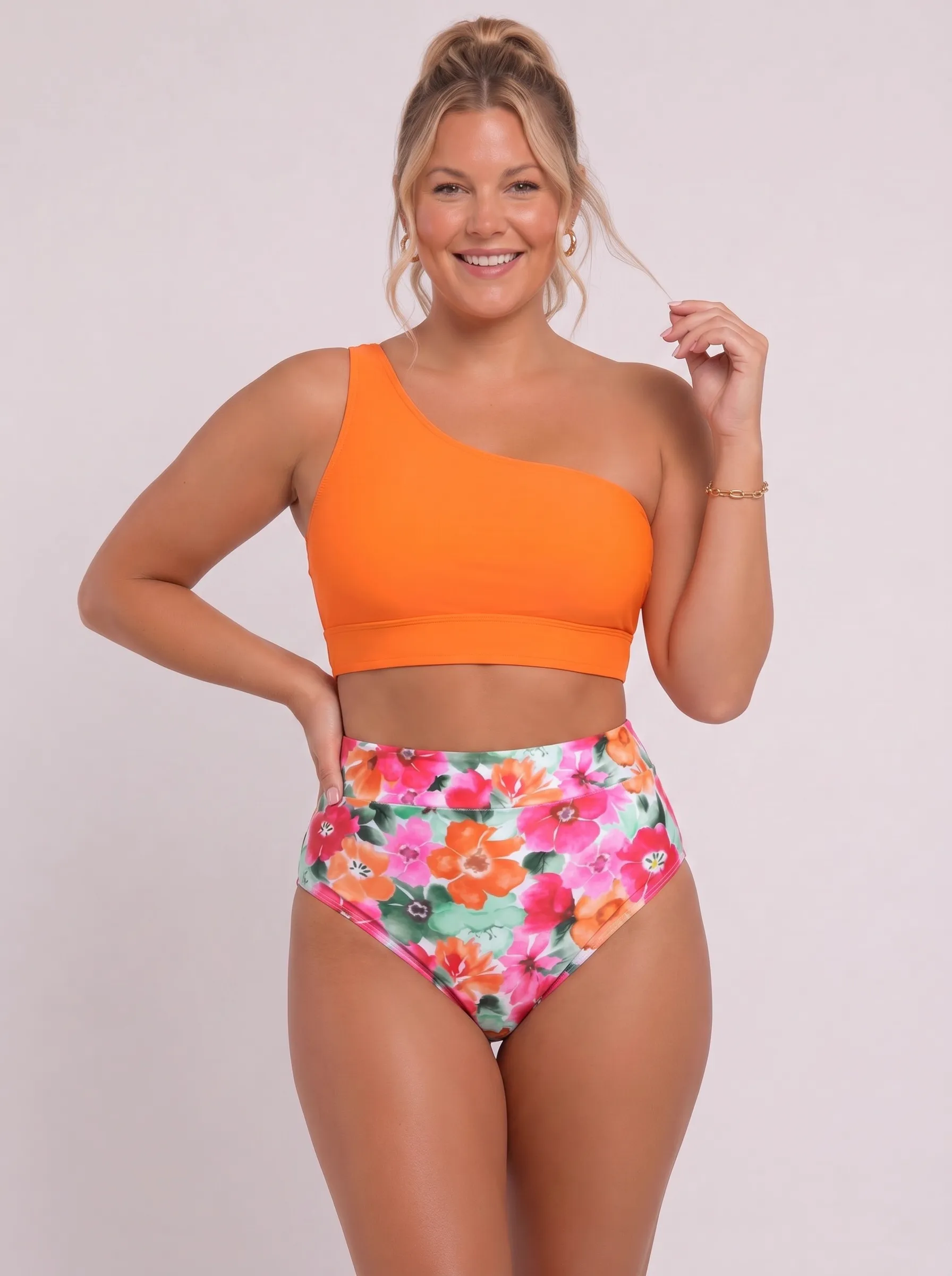 MODA AI swimwear output — plus-size blonde model in orange one-shoulder bikini top with tropical hibiscus floral high-waist bottoms, full-body smile