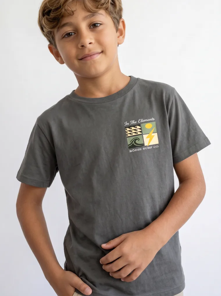 A charcoal boys tee with a surf graphic on the chest and a larger version across the back, worn with stone shorts. FW26 look 18, Graphic Basic in Charcoal, frame 1 of 5