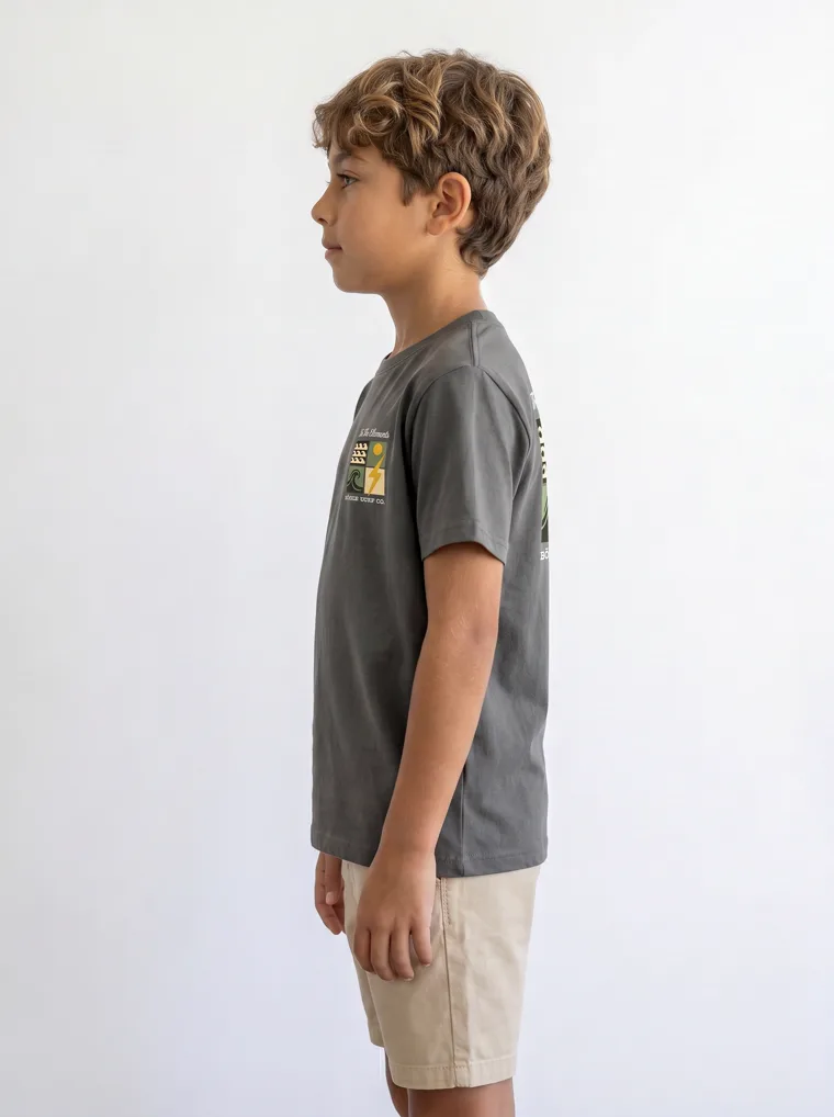 A charcoal boys tee with a surf graphic on the chest and a larger version across the back, worn with stone shorts. FW26 look 18, Graphic Basic in Charcoal, frame 4 of 5