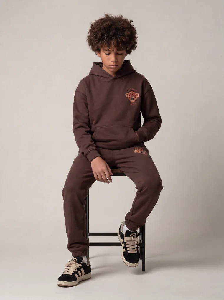 A chocolate brown kids hoodie and jogger set with a tonal animal graphic. FW26 look 20