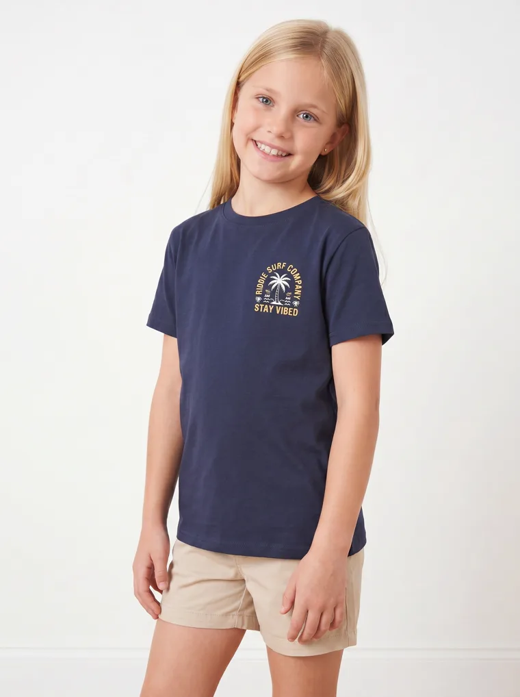 A navy girls tee with a palm and surfboard graphic, worn with stone shorts. FW26 look 19, Graphic Basic in Navy, frame 1 of 5
