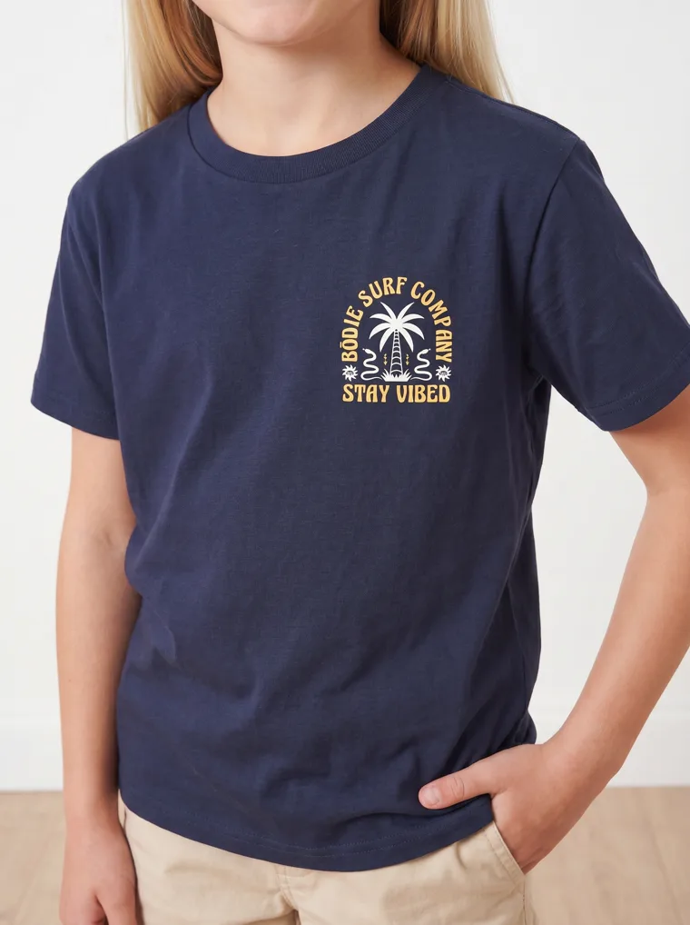 A navy girls tee with a palm and surfboard graphic, worn with stone shorts. FW26 look 19, Graphic Basic in Navy, frame 3 of 5