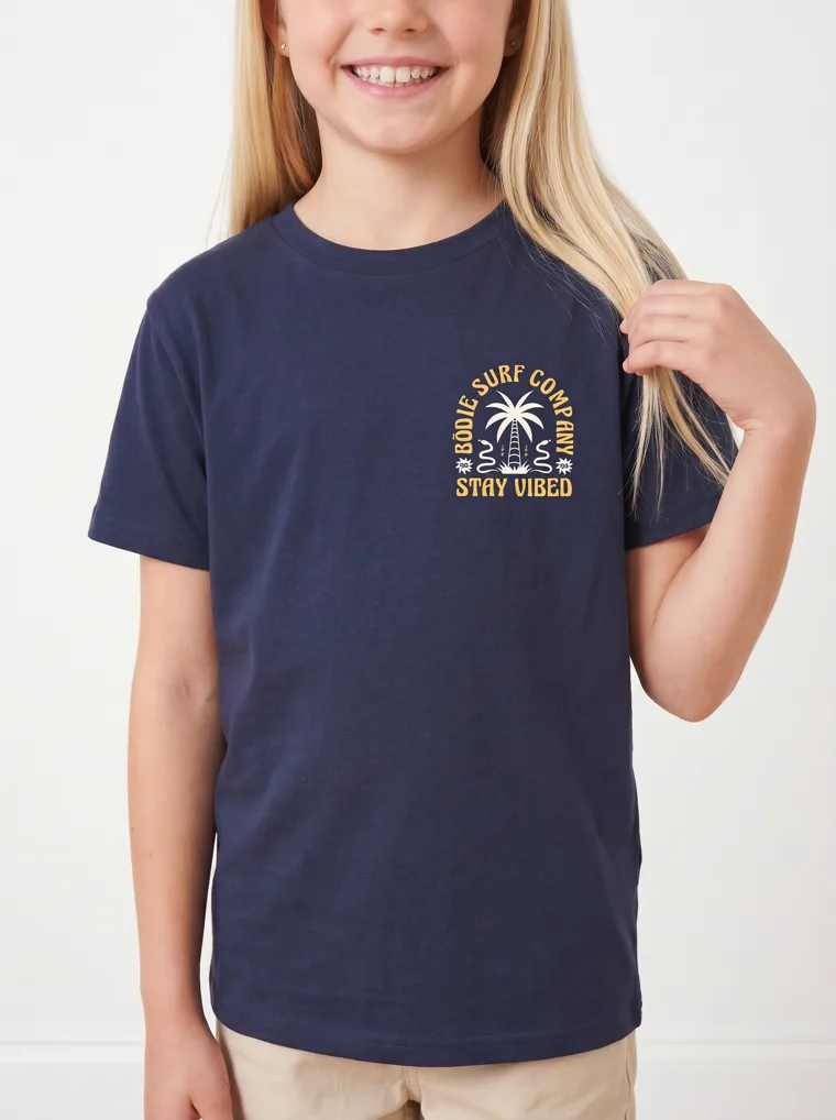A navy girls tee with a palm and surfboard graphic, worn with stone shorts. FW26 look 19, Graphic Basic in Navy, frame 5 of 5