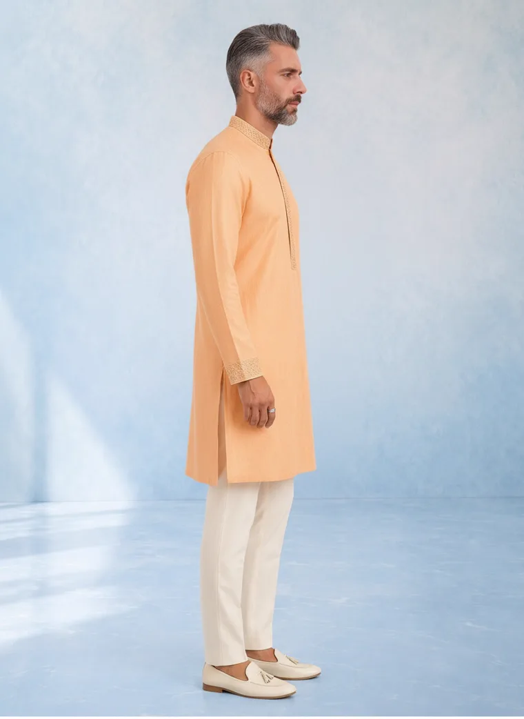 A peach kurta with cream churidar trousers and cream loafers against a pale blue painted backdrop. FW26 look 03, New Neutral in Peach, frame 3 of 5