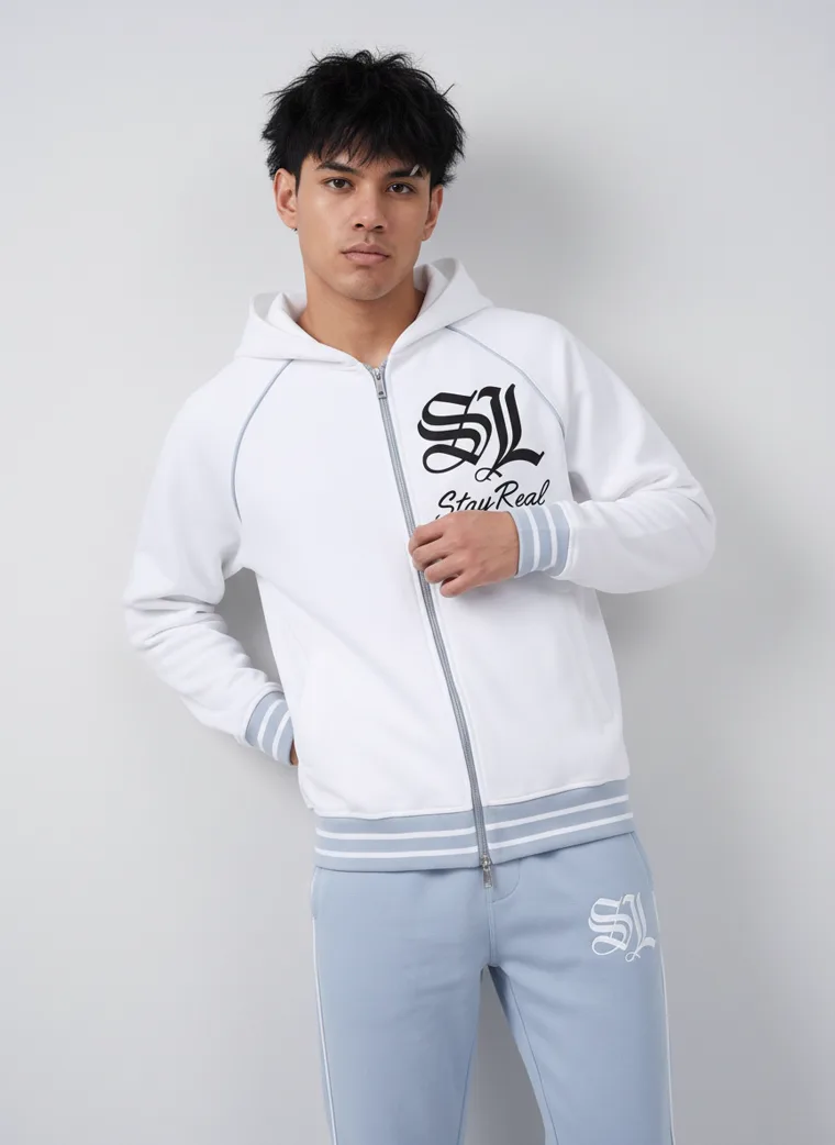 A white zip through hoodie with gothic lettering and a large back print, worn with pale blue sweatpants. FW26 look 05, Graphic Layer in White, frame 2 of 5