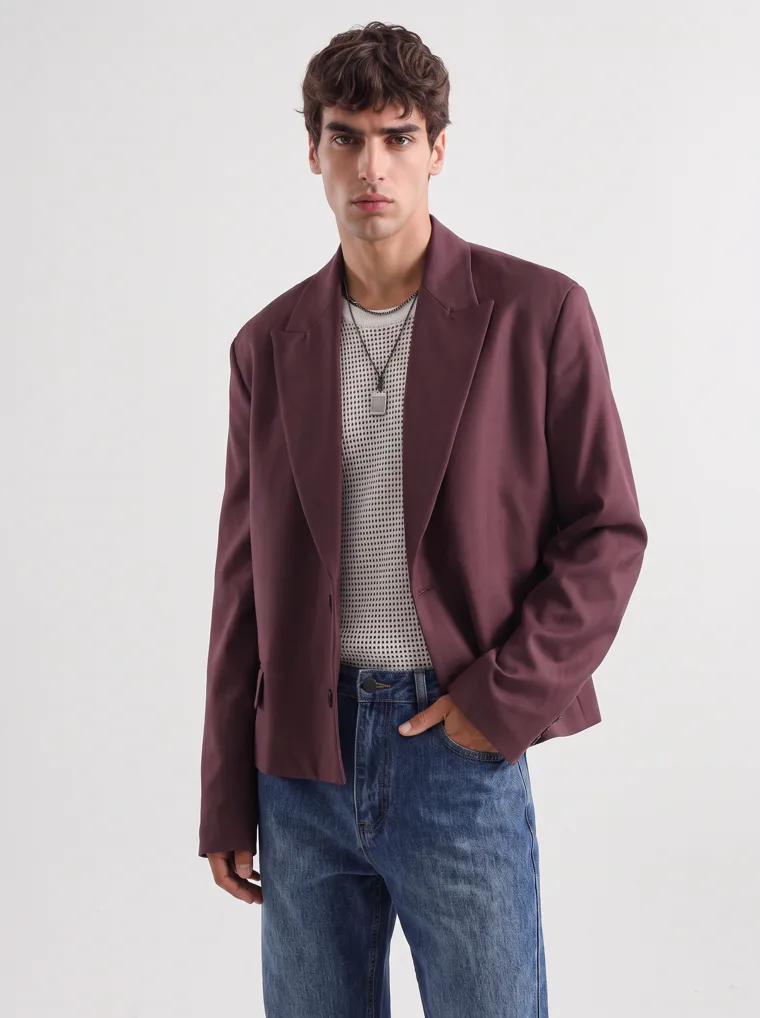 A model in an oversized burgundy blazer over a fine striped knit with straight blue jeans, FW26 look 02