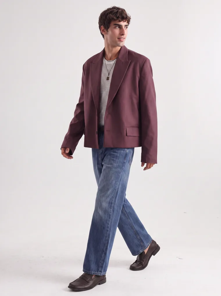 An oversized burgundy blazer over a fine striped knit with straight blue jeans and a burgundy tote. FW26 look 02, Soft Tailoring in Burgundy, frame 2 of 5