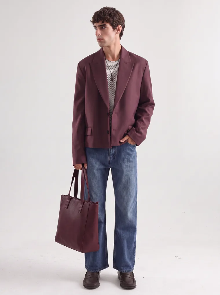 An oversized burgundy blazer over a fine striped knit with straight blue jeans and a burgundy tote. FW26 look 02, Soft Tailoring in Burgundy, frame 3 of 5
