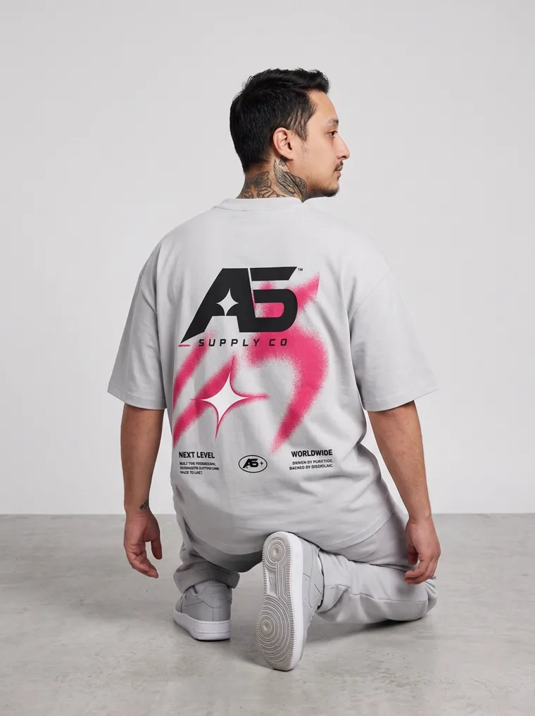 A model in an oversized light grey tee and matching grey sweatpants with a small chest logo, FW26 look 06