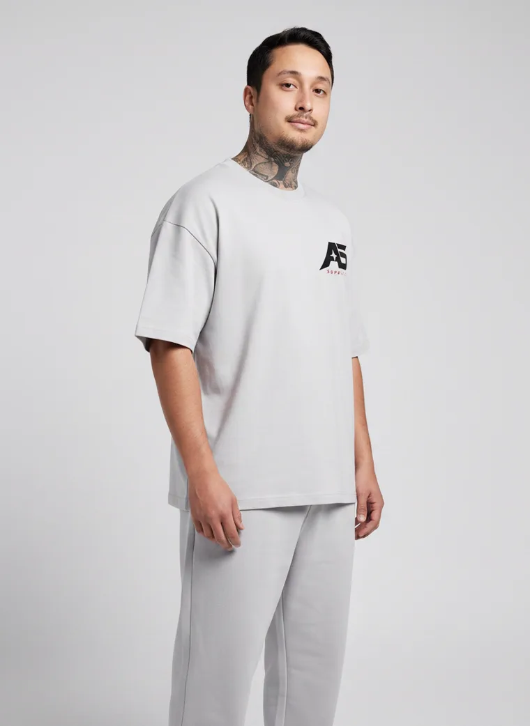 An oversized light grey tee and matching grey sweatpants with a small chest logo and a large back graphic. FW26 look 06, Tonal Sportswear in Grey, frame 3 of 5