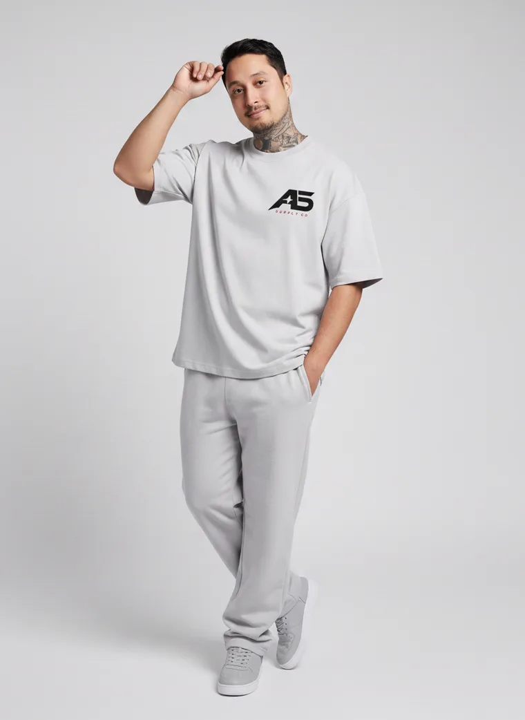 An oversized light grey tee and matching grey sweatpants with a small chest logo and a large back graphic. FW26 look 06, Tonal Sportswear in Grey, frame 4 of 5