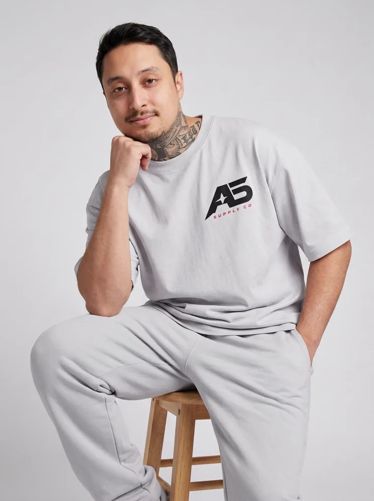 An oversized light grey tee and matching grey sweatpants with a small chest logo and a large back graphic. FW26 look 06, Tonal Sportswear in Grey, frame 5 of 5