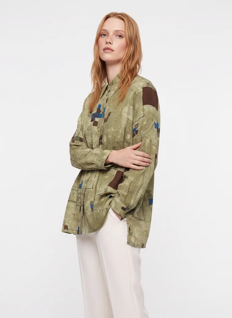 A model in an olive abstract print oversized shirt worn open over cream wide leg trousers, FW26 look 08
