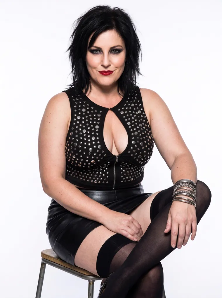 A black studded keyhole crop top with a wet-look mini skirt, sheer black stockings, stacked silver cuffs and heels, on a plus-size model against a white studio wall. Studded Keyhole Crop and Wet-Look Mini in black, frame 4 of 5