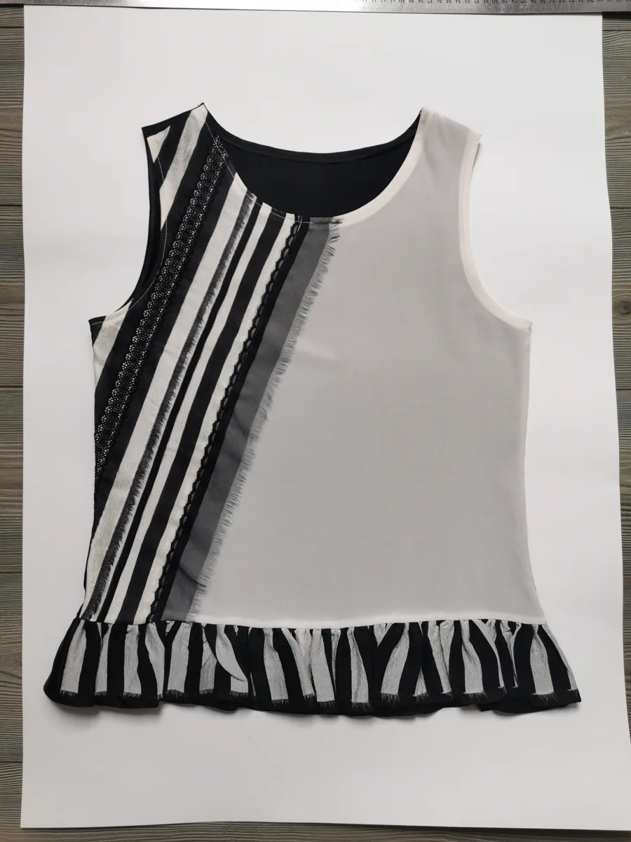 Input flat lay — sleeveless top with vertical black and cream embroidered appliqué stripes and a ruffle hem, laid flat on white