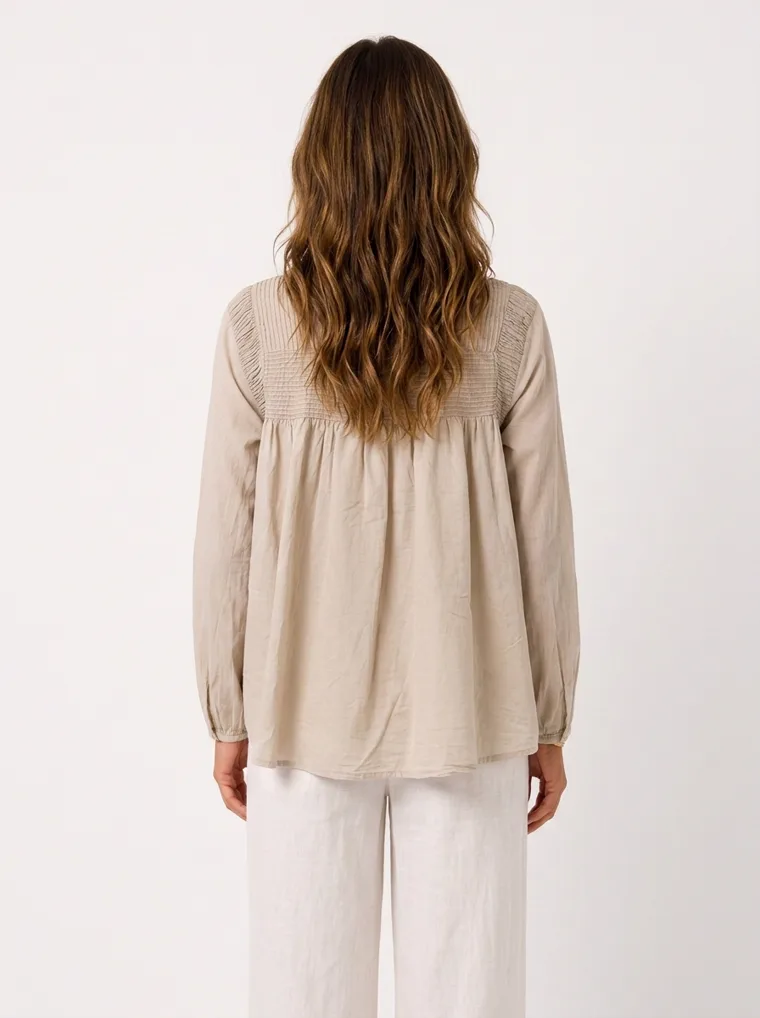 MODA AI on-model output — the oatmeal smock blouse styled with cream wide-leg trousers, back view, generated from a hanger shot in the same clean studio as the rest of the collection