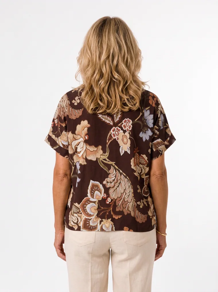 MODA AI on-model output — the brown floral short-sleeve blouse styled with cream trousers, back view, generated from a hanger shot in the same clean studio as the rest of the collection