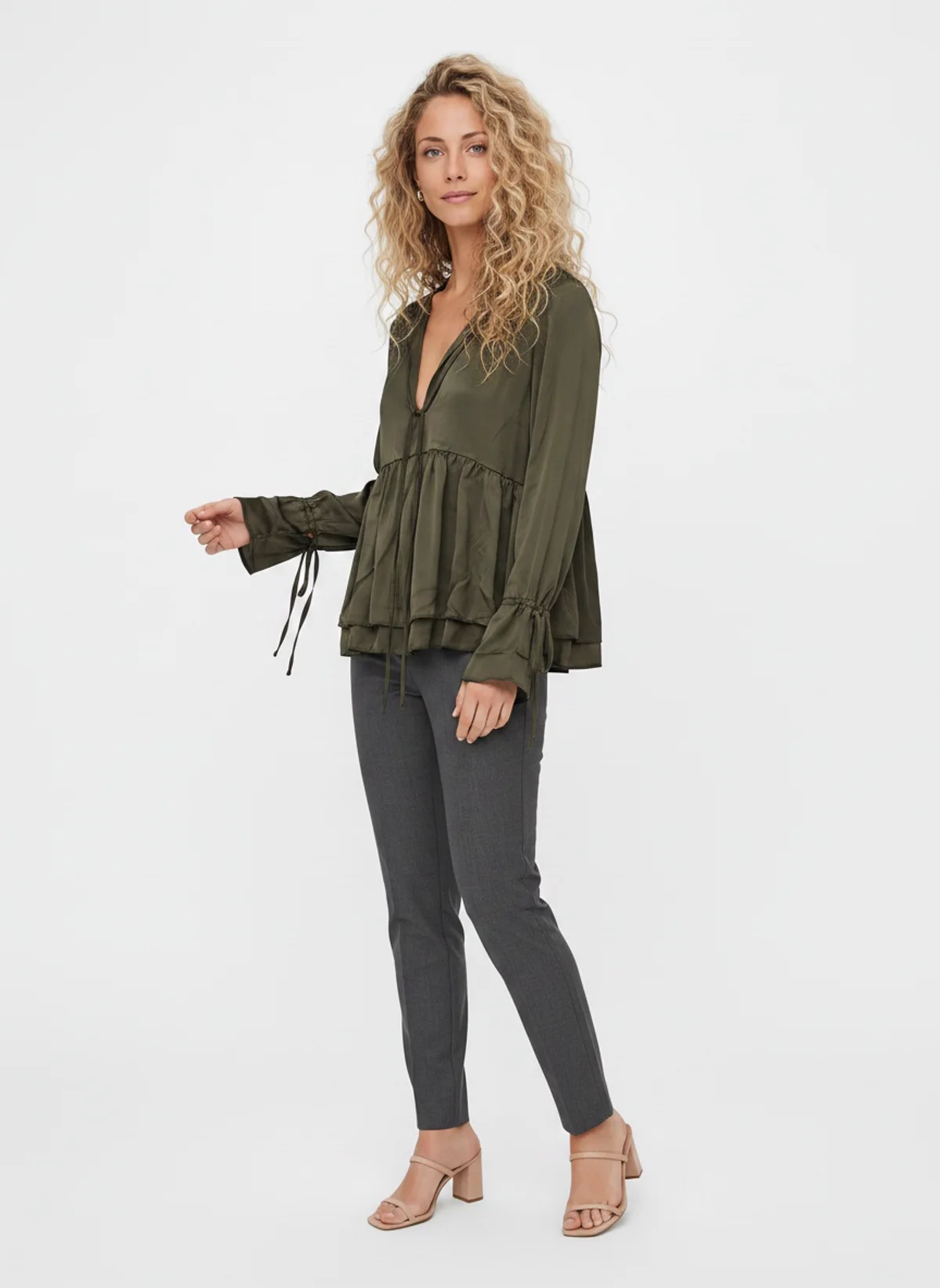 MODA AI output — a woman with curly blonde hair wearing an olive tiered blouse with grey trousers in a clean studio, generated from a photo of the blouse on a hanger