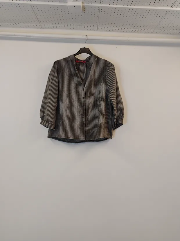 Hanger shot input — a fine-striped button-through shirt with three-quarter sleeves, hanging against a plain shop wall